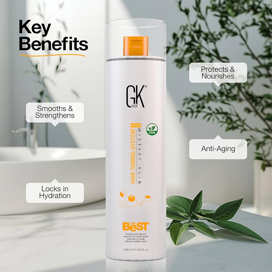 GK Hair Taming System bottle featuring key benefits: smooths and strengthens, locks in hydration, protects and nourishes, and provides anti-aging properties. Vegan formula with Juvexin, showcased in a modern bathroom setting with greenery